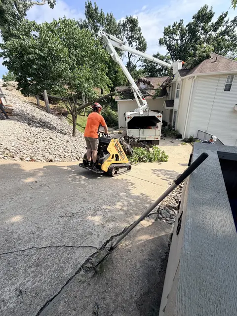 A Colt Tree Service boom truck and mini skid loader clearing storm damage from a driveway